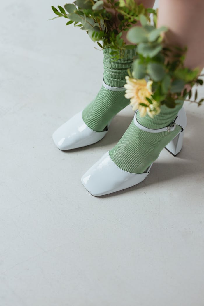 Close-up of white heels with green socks and flowers for a chic look.