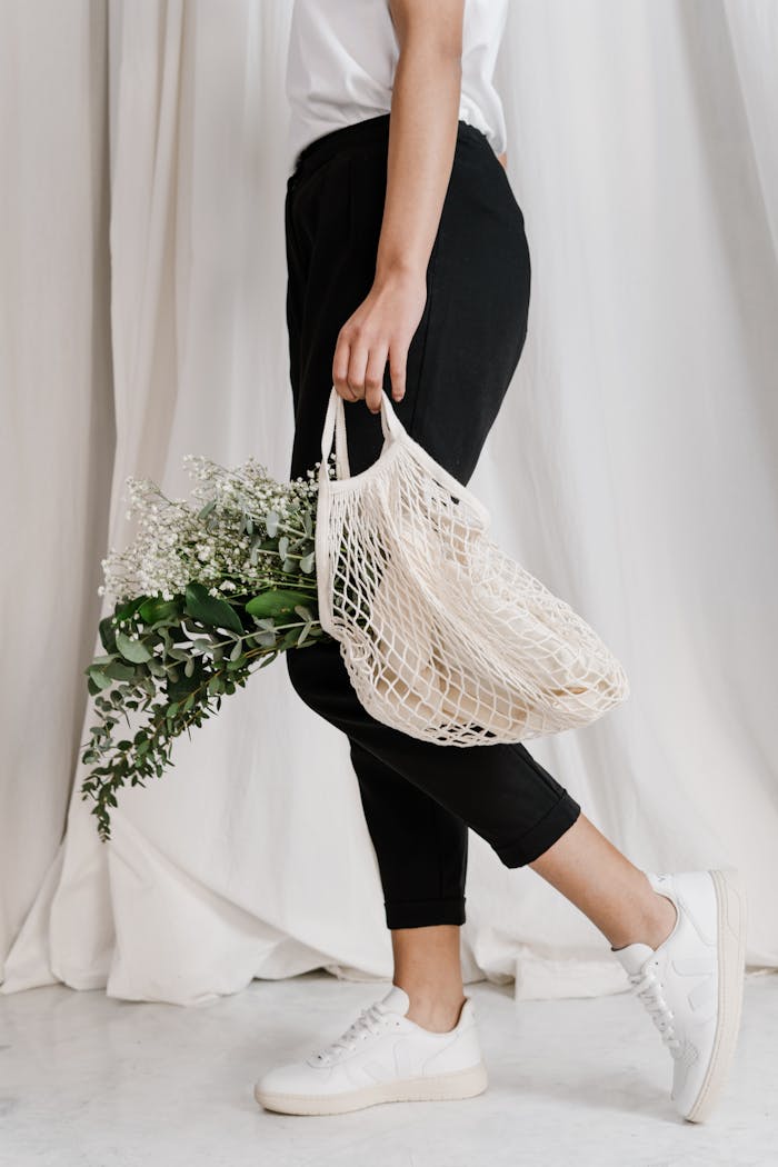 Person carrying reusable mesh bag with flowers, embracing eco-friendly lifestyle.